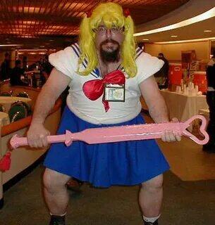 Бородатый мужчина в парике с хвостиками и костюме Sailor Moon держит розовую палочку, на заднем плане видны другие люди